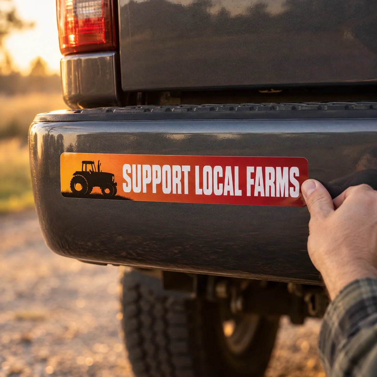 Custom full-color bumper sticker reading SUPPORT LOCAL FARMS being pressed onto the rear bumper of a gray pickup truck