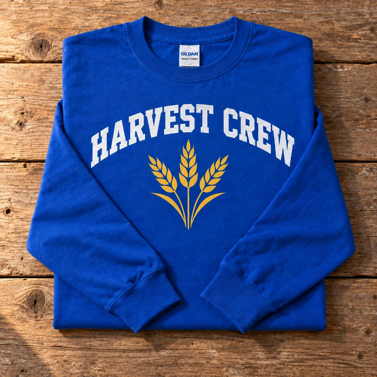 Custom Gildan Heavy Cotton long sleeve t-shirt in Royal with a full-color HARVEST CREW wheat DTF print, folded on a wood table