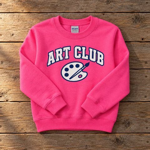 Custom Gildan Heavy Blend youth crewneck sweatshirt in Safety Pink with a full-color ART CLUB DTF print, folded on a wood table