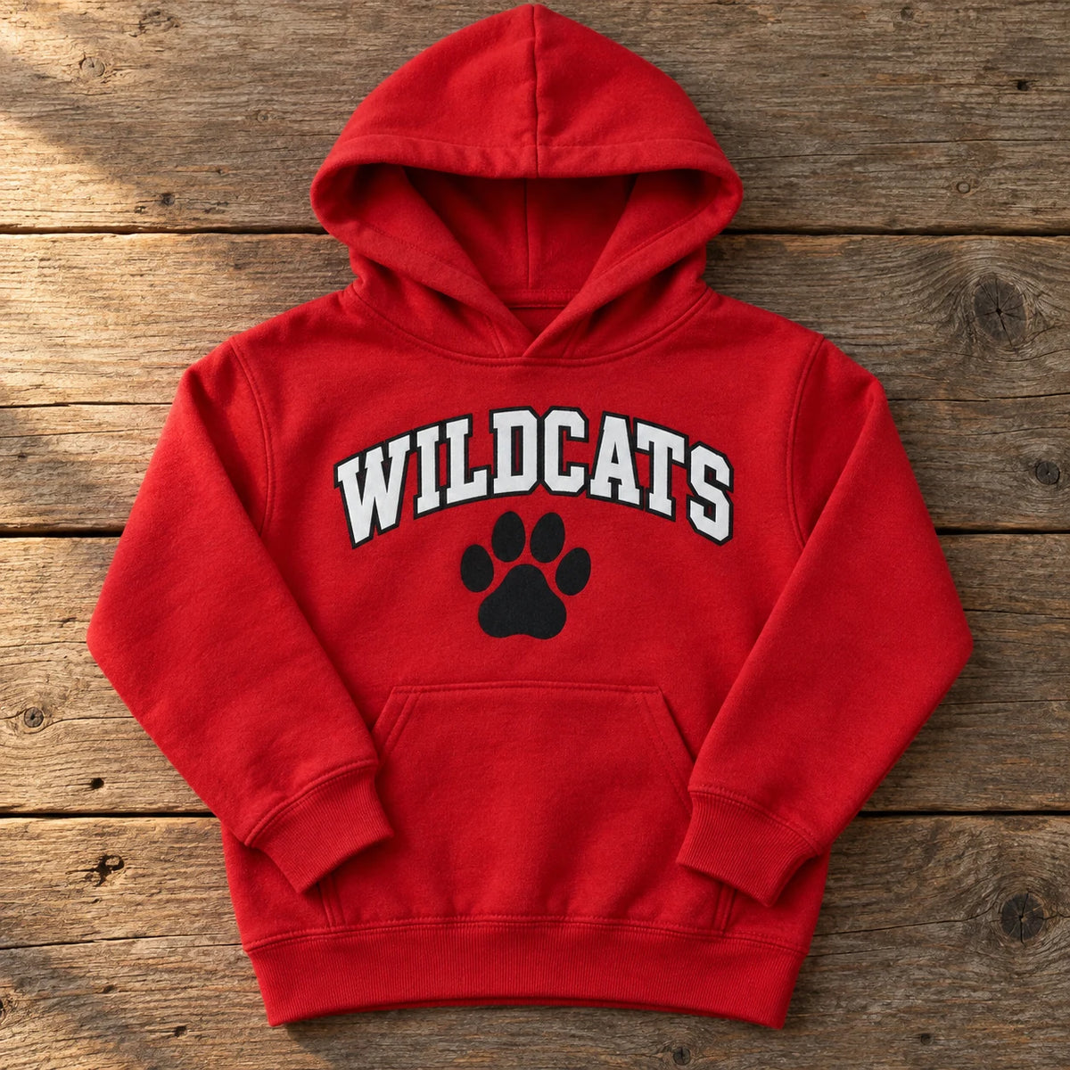 Custom Gildan Heavy Blend youth hoodie in Red with a full-color WILDCATS paw print DTF design, folded on a wood table