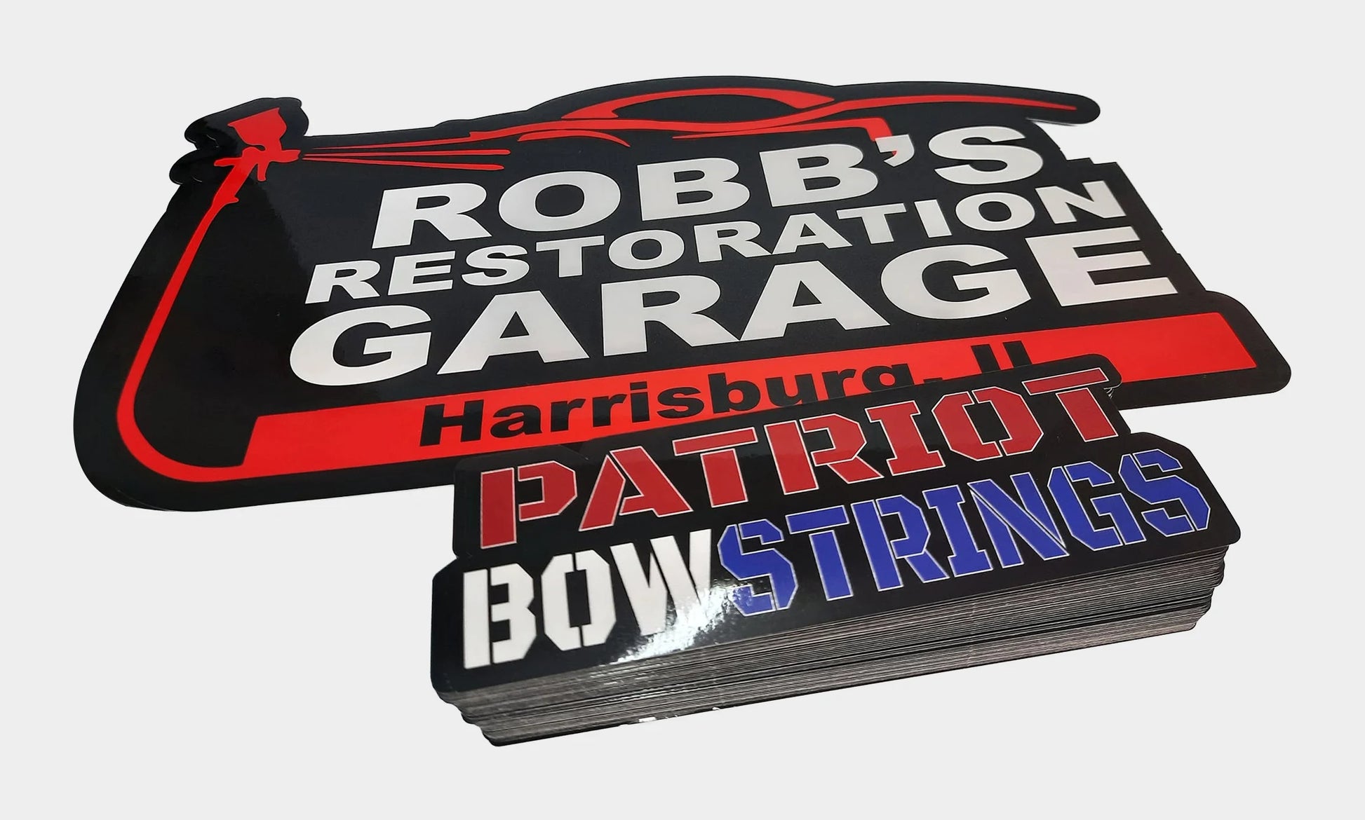 Custom die cut vinyl stickers cut in our shop - a restoration garage logo decal and a thick stack of red white and blue laminated stickers
