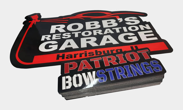 Custom die cut vinyl stickers cut in our shop - a restoration garage logo decal and a thick stack of red white and blue laminated stickers
