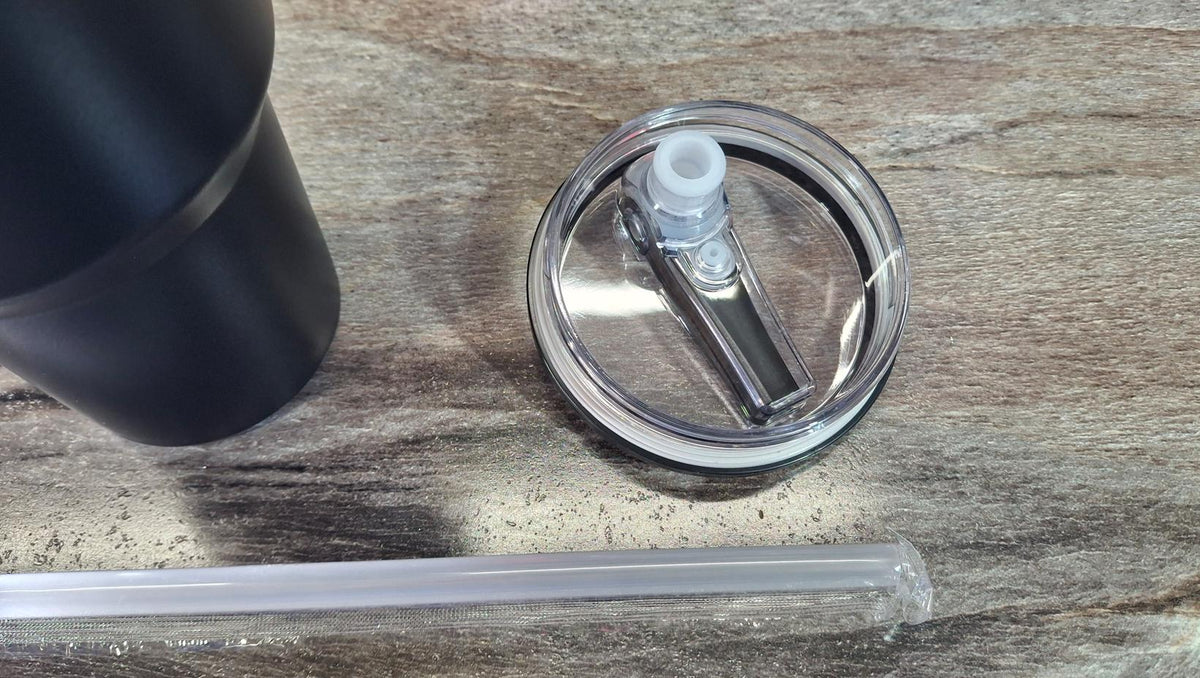 The tumbler's clear flip lid and straw beside a Black tumbler