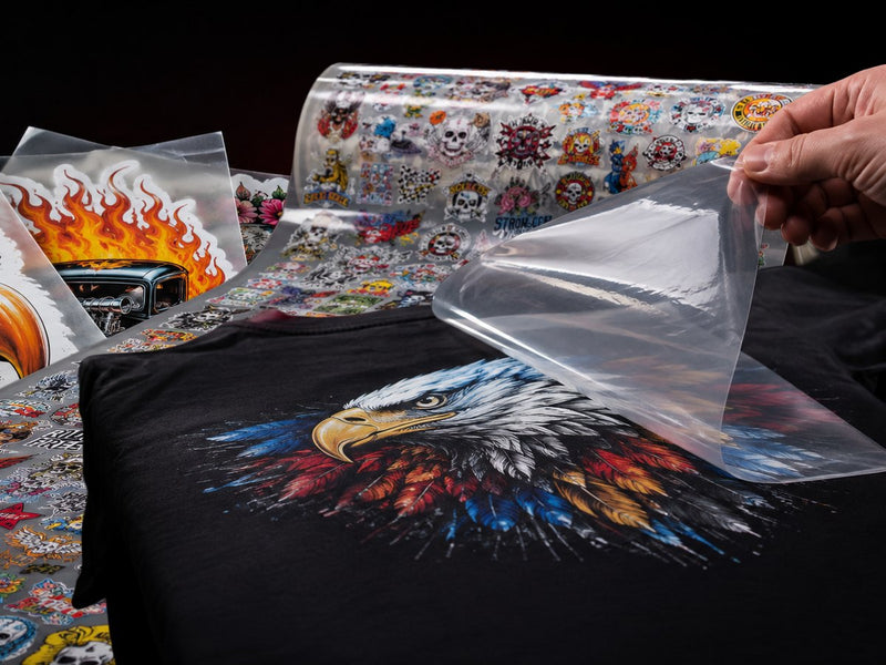 DTF transfer peeling off a printed shirt beside gang sheet rolls